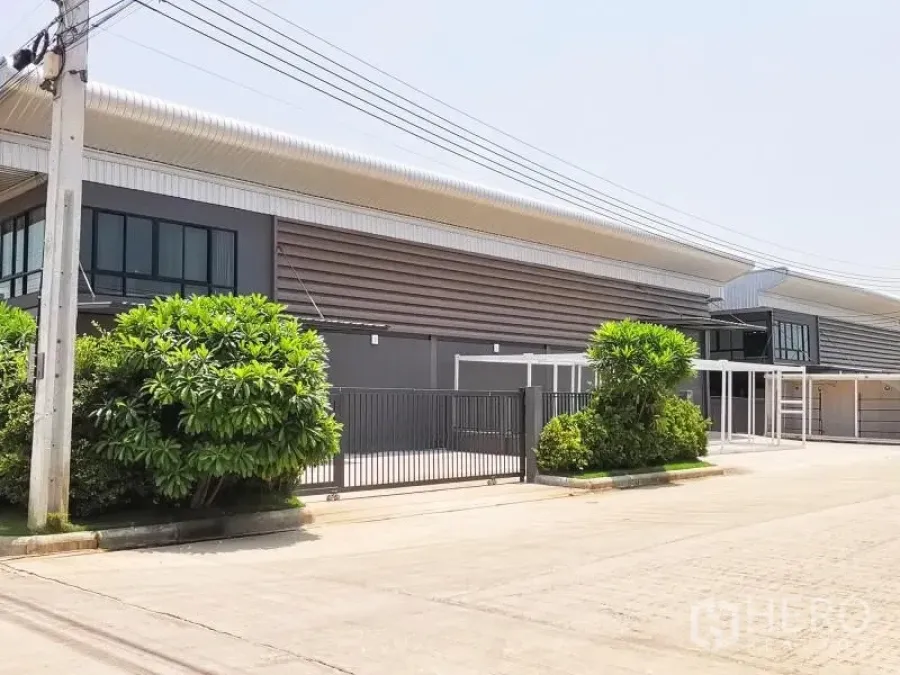 Factory for rent or sale in Bang Bo, Samut Prakan - Street view of a gated industrial compound with landscaped frontage and a long-span roof.