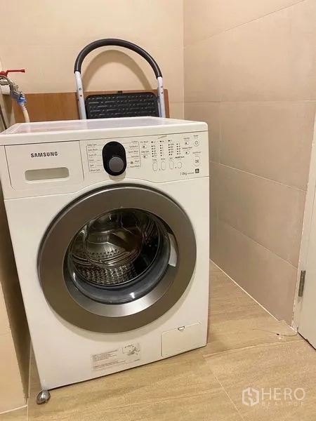 公寓 出租或出售在Bang Kapi, Bangkok - 洗衣角落，滚筒洗衣机置于米色瓷砖地面上。