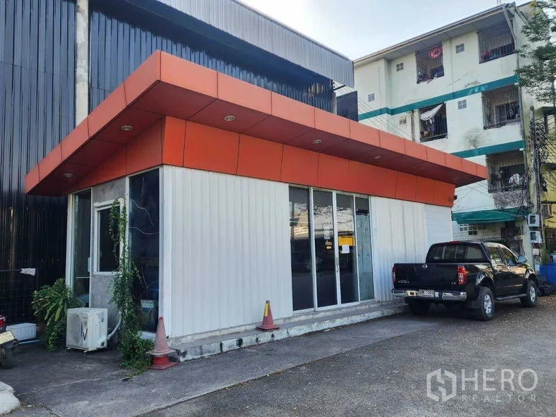 货栈 出租在Lat Phrao, Bangkok - 仓库旁的办公室外观斜角，推拉玻璃门与停车区。