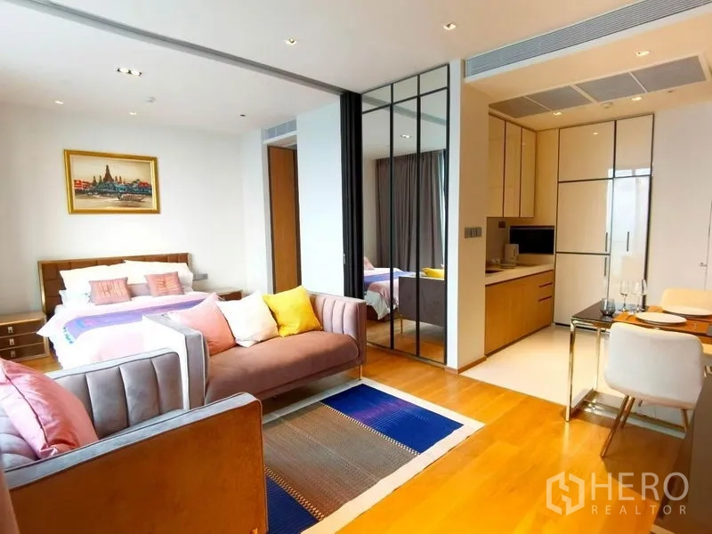 Condominium for rent in Khlong Toei, Bangkok - Bright open-plan condo with bed, sofa seating, kitchenette, and mirrored partition on wooden floors.