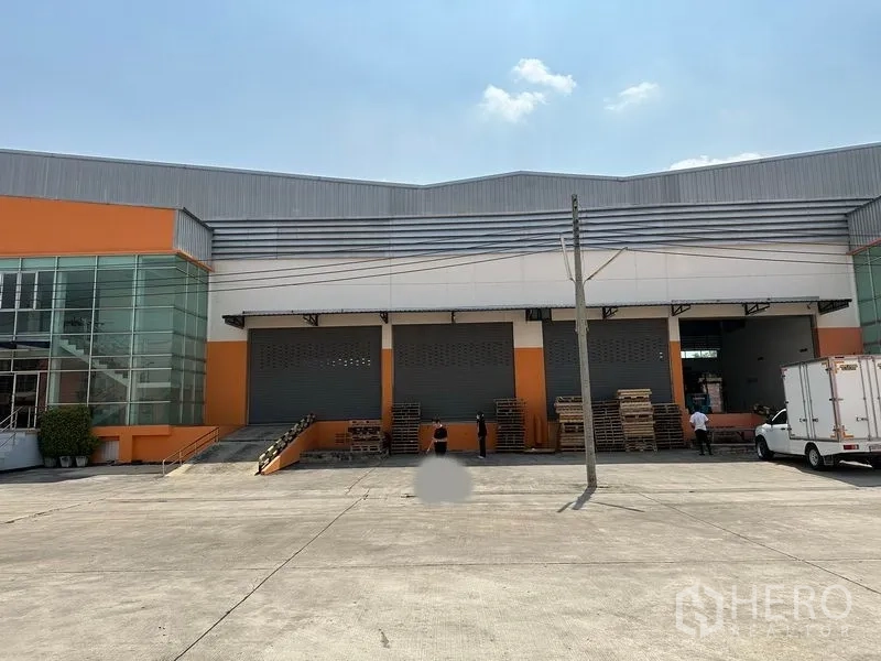 Warehouse for rent in Mueang Samut Prakan, Samut Prakan - Front loading dock showing several roller shutters and a wide concrete yard for truck maneuvering.