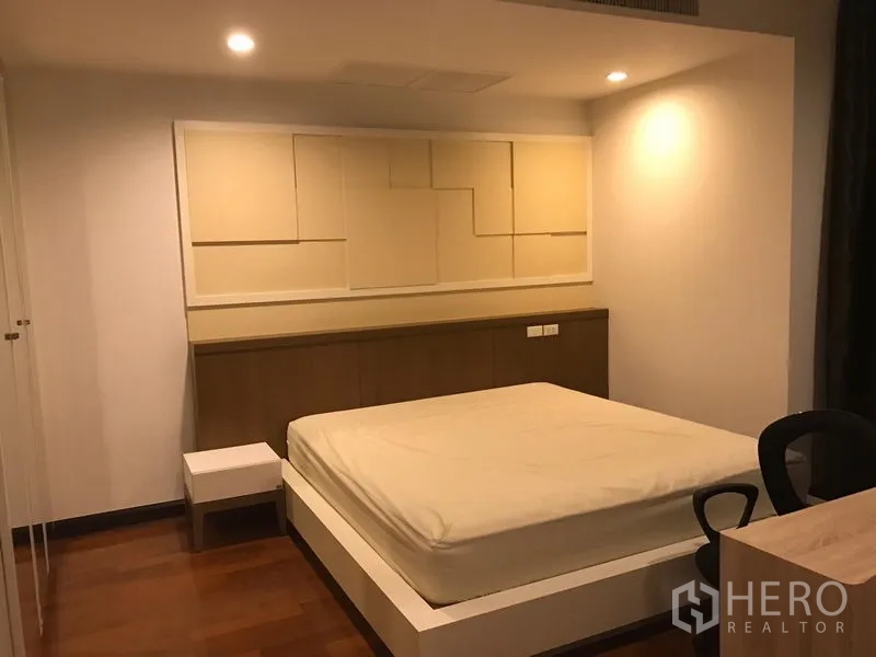 คอนโด ให้เช่าในWatthana, Bangkok - ห้องนอนหลักพร้อมเตียงยกพื้น พื้นไม้ ผนังหัวเตียงลายพาเนล และไฟดาวน์ไลท์อบอุ่น