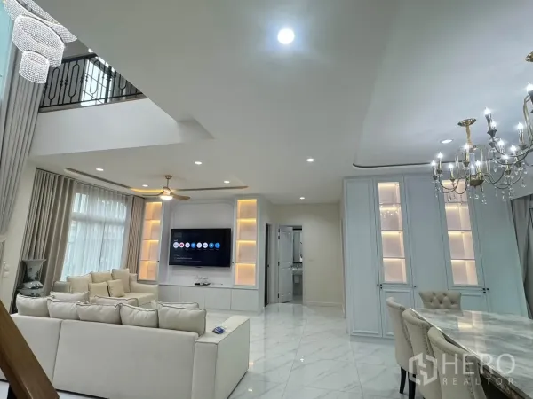 Detached House for rent or sale in Bang Phli, Samut Prakan - Open-plan living and dining area with double-height ceiling, chandelier, built-in TV wall and light sofas on marble-look floors.