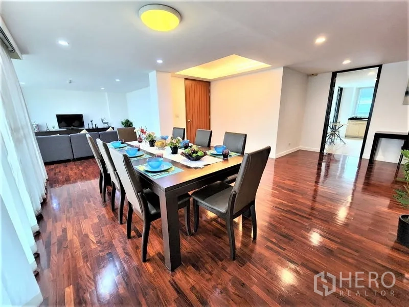 Condominium for rent in Bang Rak, Bangkok - Open-plan dining and living area with a long table, large windows with sheer curtains, recessed lighting and polished hardwood floors.
