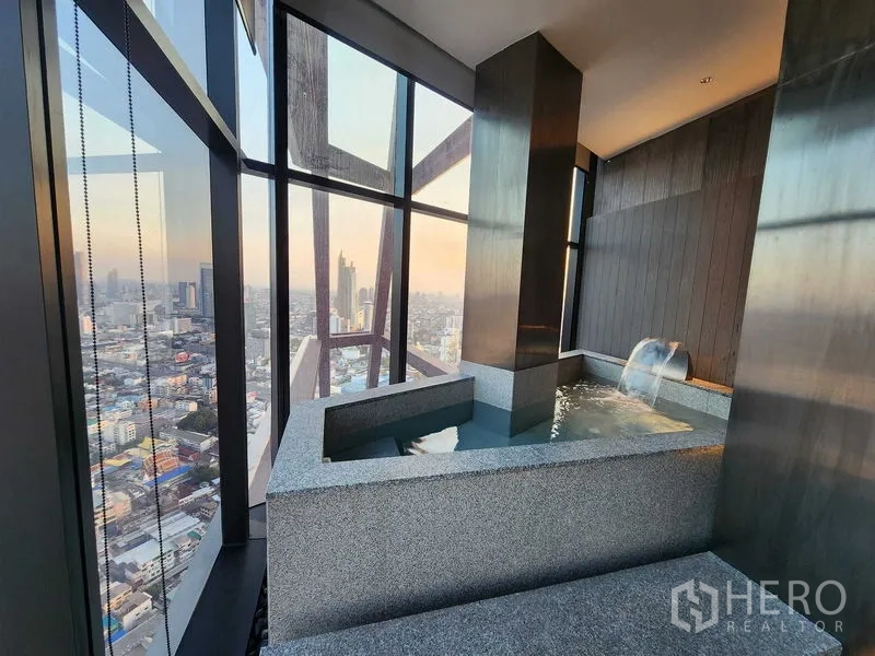 Condominium for rent - Indoor onsen-style hot tub with waterfall spout and expansive city views through large windows.
