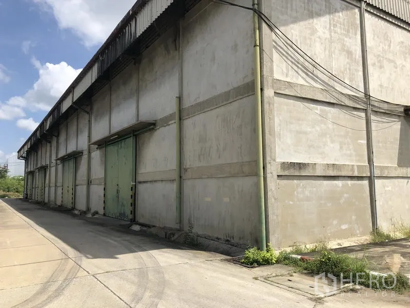 Warehouse for rent in Mueang Pathum Thani, Pathum Thani - Side view of long warehouse block showing multiple loading bays and a wide truck-friendly driveway.