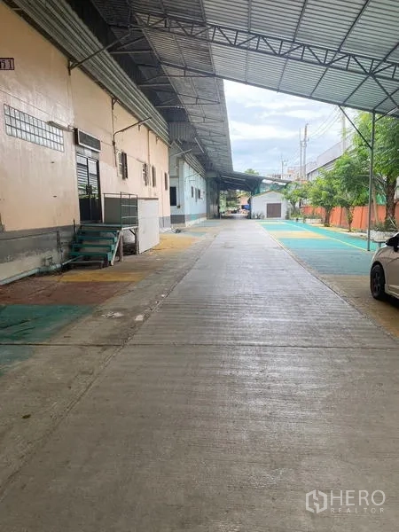 Warehouse for rent in Lam Luk Ka, Pathum Thani - Long covered loading corridor beside warehouse with trees and parking