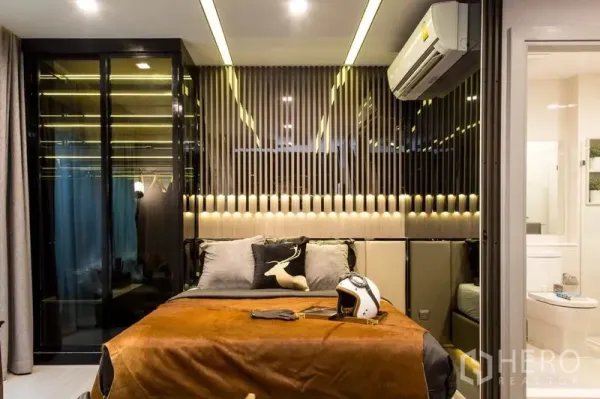 公寓 出售在Ratchathewi, Bangkok - 温馨卧室，软包床头、竖条装饰墙、玻璃衣柜与套内卫浴。