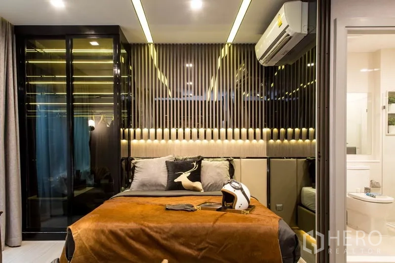 公寓 出售在Ratchathewi, Bangkok - 温馨卧室，软包床头、竖条装饰墙、玻璃衣柜与套内卫浴。