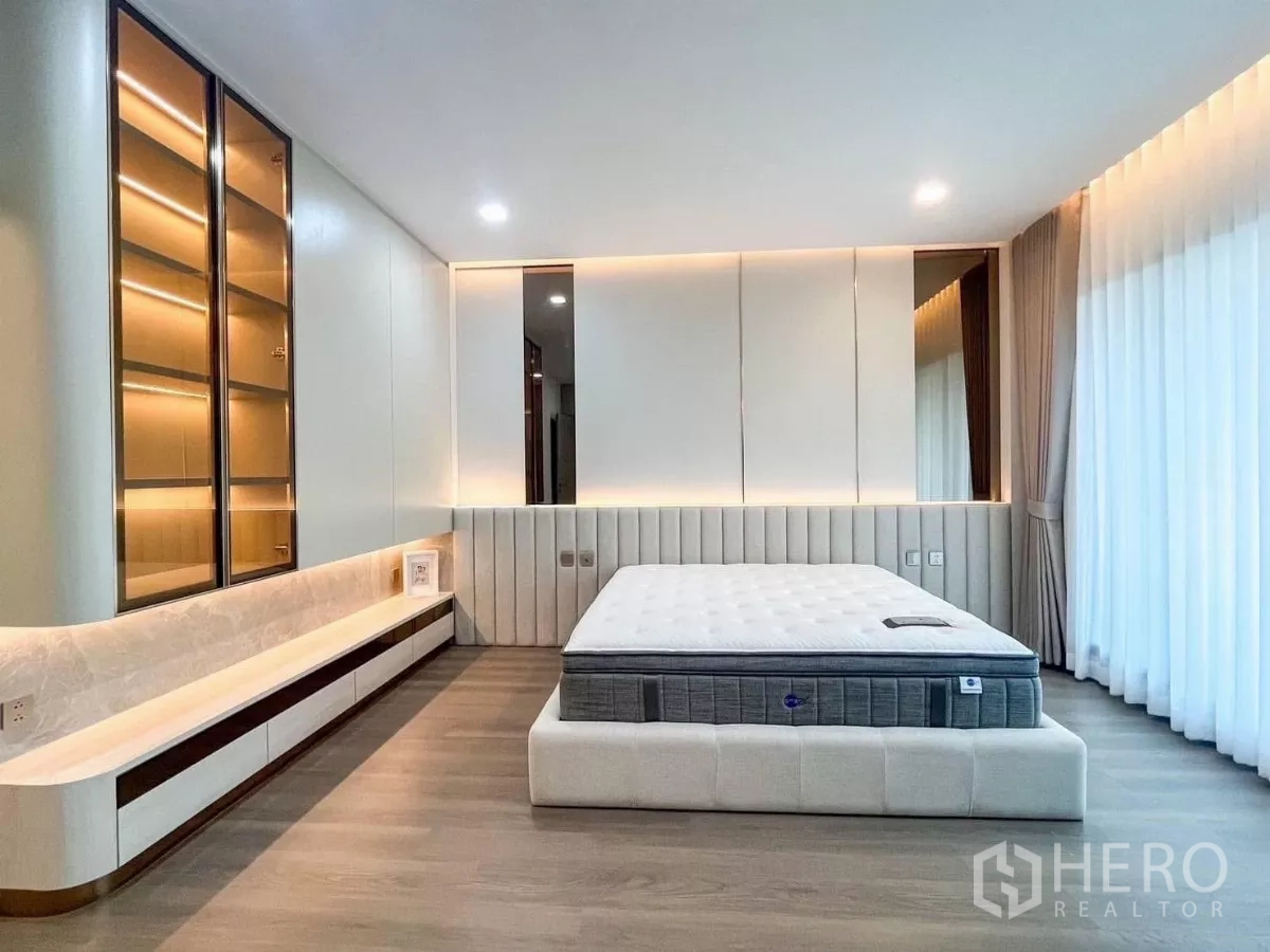 Detached House for rent or sale in Prawet, Bangkok - Master bedroom with upholstered bed, built-in shelves, mirrored headboard and full-height curtains.