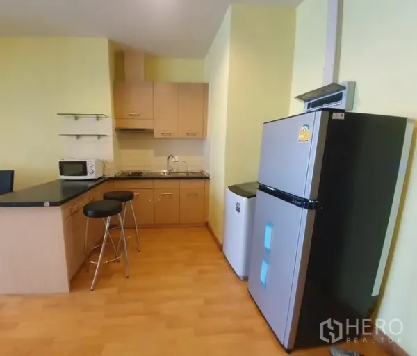 Condominium for rent in Khlong Toei, Bangkok - Compact open kitchen with breakfast bar, cabinets, cooktop, microwave and full-size refrigerator.