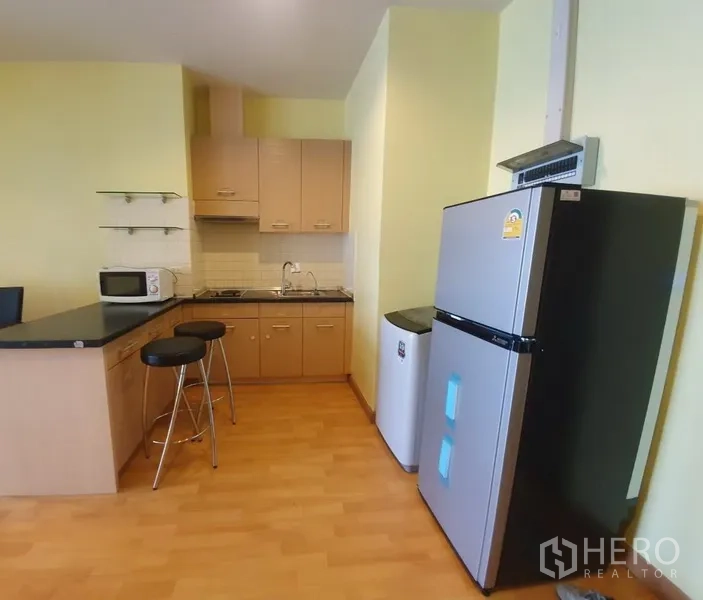 Condominium for rent in Khlong Toei, Bangkok - Compact open kitchen with breakfast bar, cabinets, cooktop, microwave and full-size refrigerator.