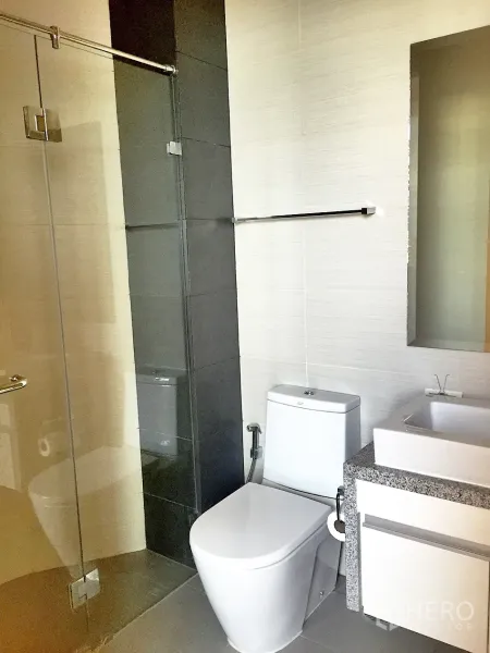 Condominium for rent in Khlong Toei, Bangkok - Contemporary bathroom featuring a glass-enclosed shower, vanity and toilet.