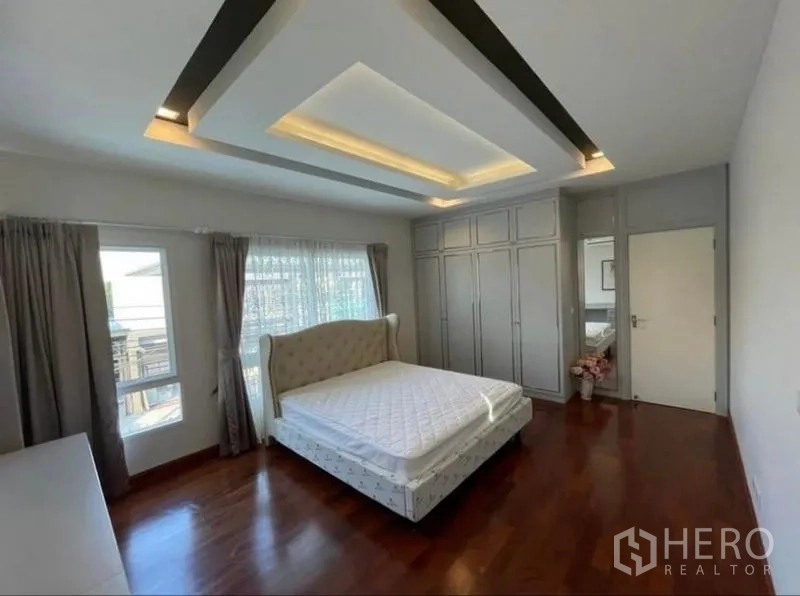 Detached House for rent or sale in Bang Phli, Samut Prakan - Bedroom with large bed, wall of built-in wardrobes, wood flooring and windows on two sides.