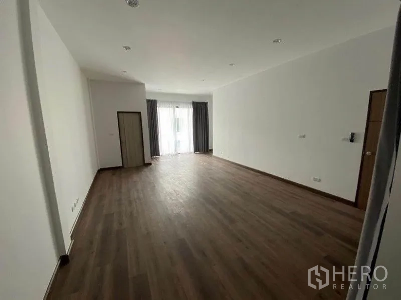 Townhouse for rent in Bang Na, Bangkok - Extra-large living space with wood flooring opening to a balcony through glass doors.