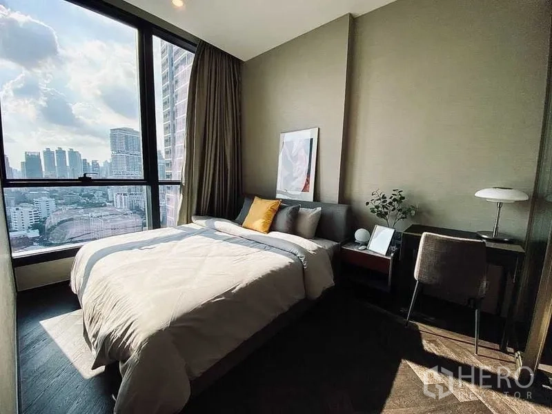 Condominium for rent in Khlong Toei, Bangkok - Cozy bedroom with large floor-to-ceiling window showcasing Bangkok skyline views.