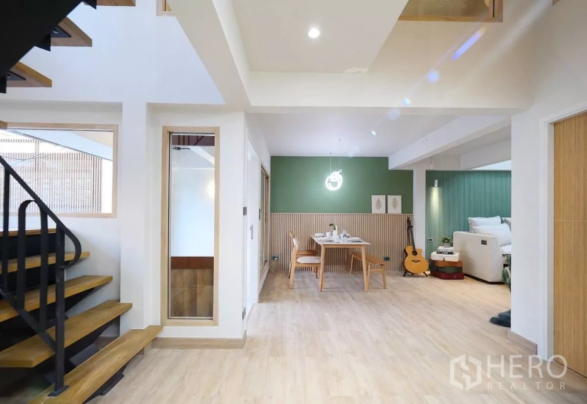 Townhouse for rent in Watthana, Bangkok - Open-plan ground floor featuring stairs, a dining nook with green feature wall and an adjacent sleeping area.
