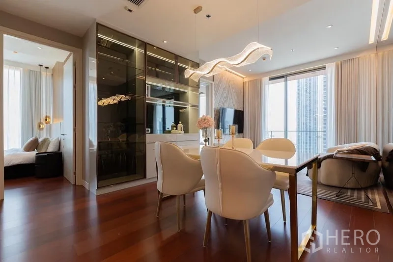 Condominium for rent in Watthana, Bangkok - Open‑plan living and dining room with glass cabinets, designer lighting and sliding doors to the balcony.