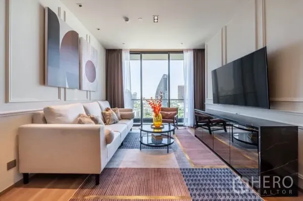 Condominium for rent in Khlong Toei, Bangkok - Living area facing a large TV and balcony with city skyline view.