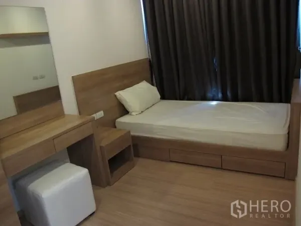 Condominium for rent or sale in Khlong Toei, Bangkok - Cozy second bedroom with single bed, vanity desk, warm wood finishes, and blackout curtains.