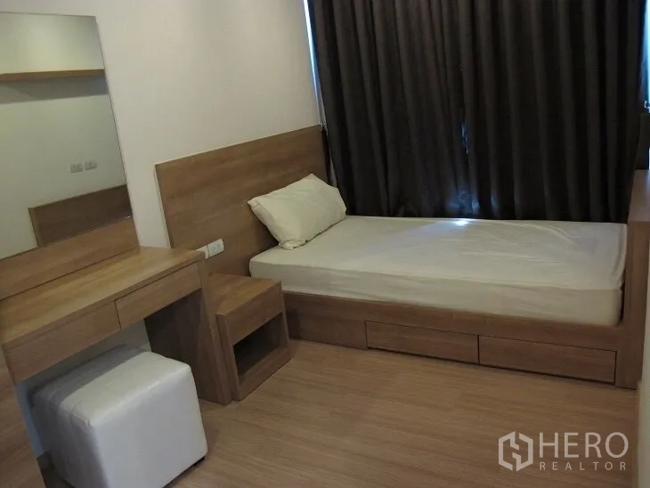 Condominium for rent or sale in Khlong Toei, Bangkok - Cozy second bedroom with single bed, vanity desk, warm wood finishes, and blackout curtains.