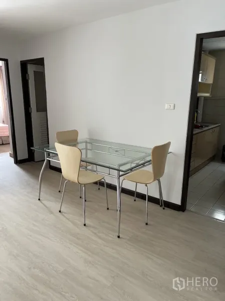 Condominium for rent or sale in Watthana, Bangkok - Dining area with a glass table and four chairs beside the separate kitchen.