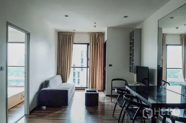 Condominium for rent in Khlong Toei, Bangkok - Bright living room with gray sofa, floor-to-ceiling window and mirror wall in a Bangkok condo.