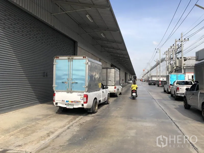 Warehouse for rent in Lam Luk Ka, Pathum Thani - Covered loading bay with large roller shutter and parked delivery trucks at a modern warehouse in Lam Luk Ka.