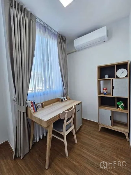 Townhouse for rent in Bang Phli, Samut Prakan - Bright study corner with wooden desk, chair, bookshelf, air conditioner and a curtained window.