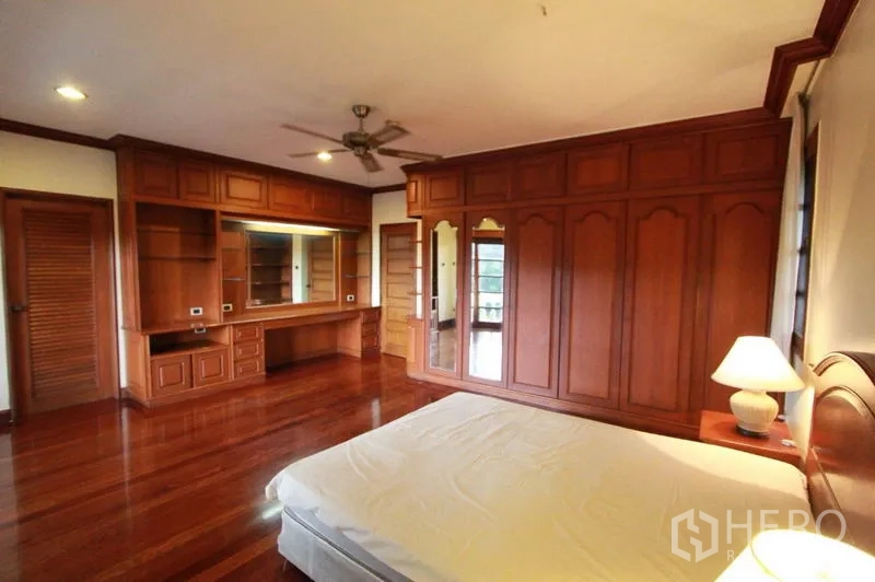 独立式住宅 出租在Prawet, Bangkok - 主卧展示整面衣柜、梳妆台、吊扇与木质地板。