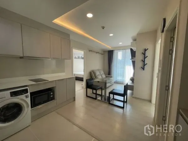 Condominium for rent in Khlong Toei, Bangkok - Open-plan kitchen and lounge with ceiling lighting and balcony window beside the bedroom doorway.
