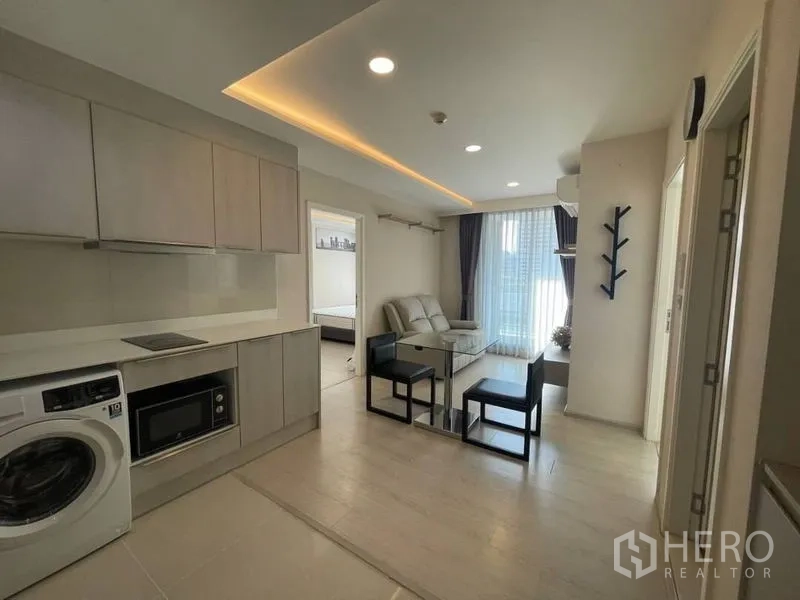 Condominium for rent in Khlong Toei, Bangkok - Open-plan kitchen and lounge with ceiling lighting and balcony window beside the bedroom doorway.