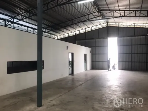 Warehouse for rent in Wang Thonglang, Bangkok - Spacious warehouse interior with steel truss roof, large sliding metal doors, concrete floor and an internal office block.