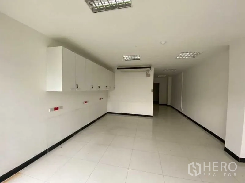 Retail Space for rent - Long workspace with wall cabinets, bright tiles and grid ceiling lights.
