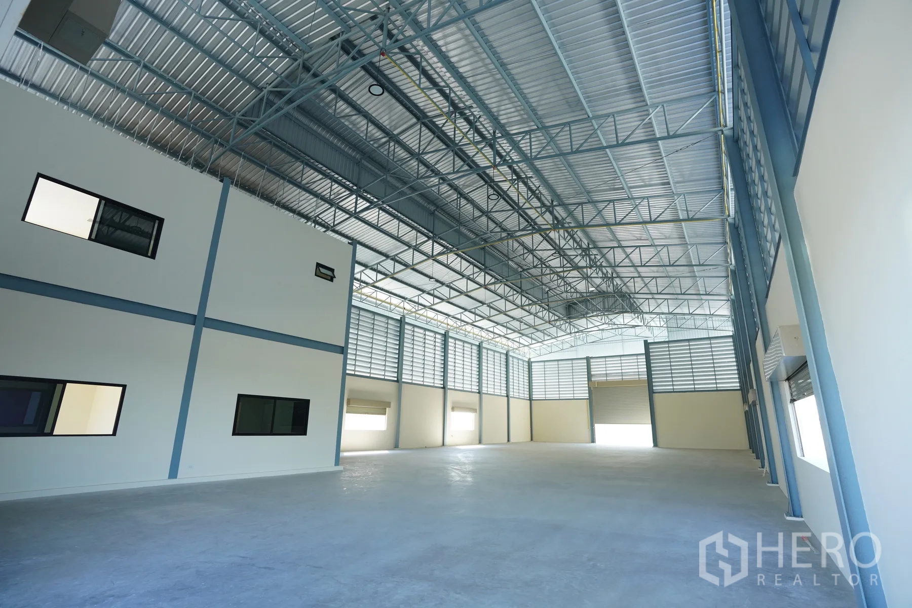 Factory for rent in Mueang Samut Prakan, Samut Prakan - Spacious factory hall with high steel truss roof, louvered vents, and attached office block.