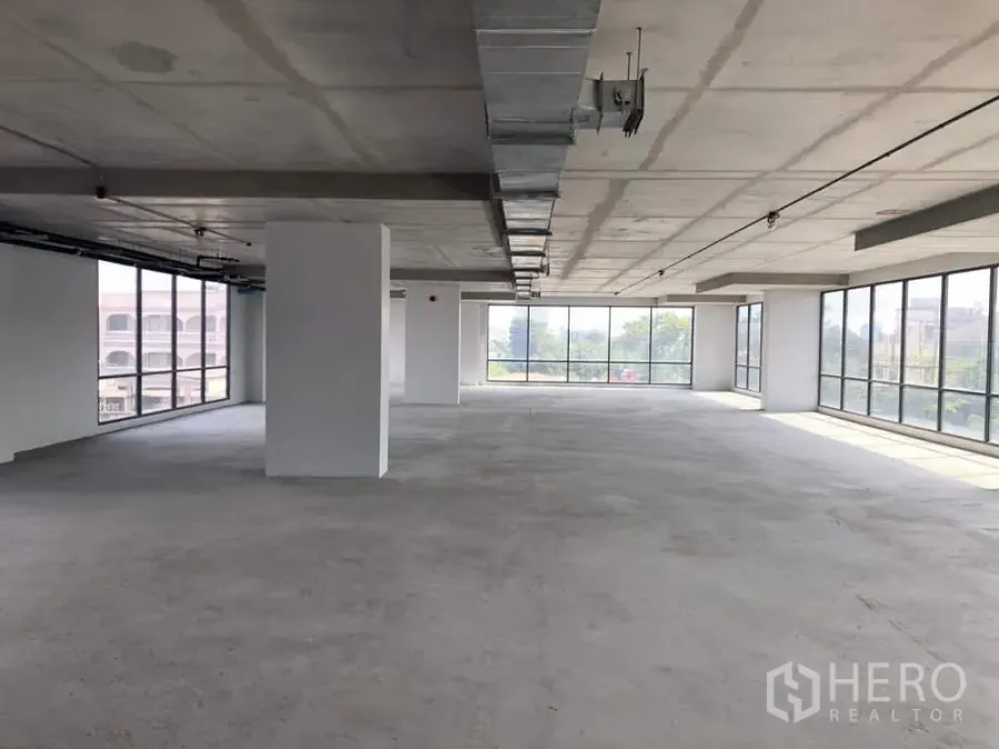 Office Space for rent in Suan Luang, Bangkok - Open-plan shell office with exposed ceiling ducts and floor-to-ceiling wraparound windows providing ample light.