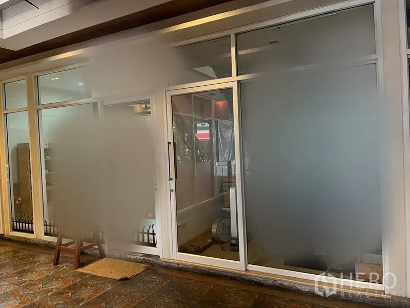 Retail Space for rent in Khlong Toei, Bangkok - Retail unit exterior with large frosted glazing, sliding entrance door, recessed ceiling lights, and stone-tiled floor.
