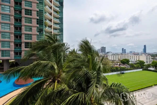 Condominium for rent in Bang Kho Laem, Bangkok - Condominium exterior with turquoise glass balconies, palm trees, curved swimming pool, and distant Bangkok skyline over a green field.
