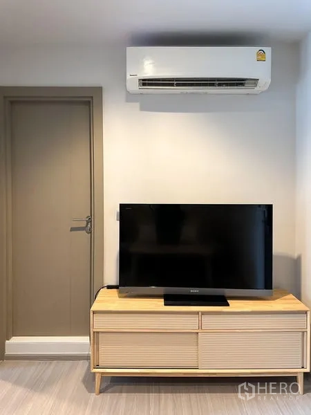 公寓 出售在Ratchathewi, Bangkok - 空调下方的浅木电视柜与电视，旁有室内门。