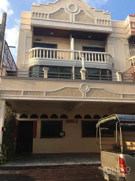 Home Office for rent in Bang Na, Bangkok - Three-storey home office facade in Bang Na with covered carport, curved balcony railings, and a beige exterior on an urban street.