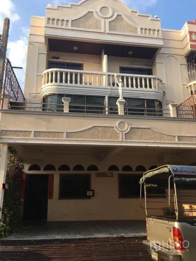 带办公室的家 出租在Bang Na, Bangkok - 三层米色外立面的家庭办公楼，带遮蔽车位与弧形阳台，位于邦那街景。
