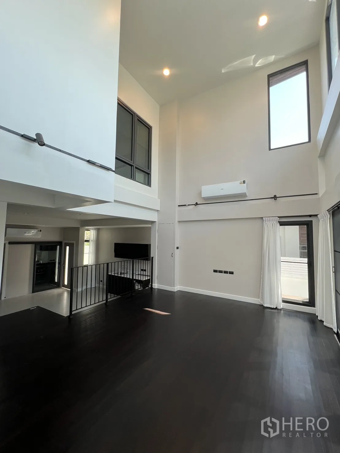 Detached House for rent in Saphan Sung, Bangkok - High-ceiling room with tall windows, white walls and dark timber floor.