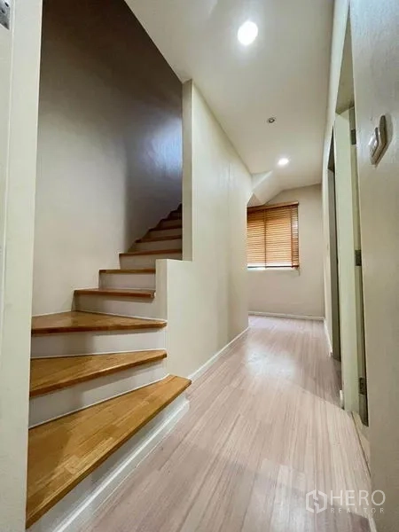 Townhouse for sale in Bang Kapi, Bangkok - Staircase with wooden steps and a corridor lit by recessed lights leading to the bedrooms.