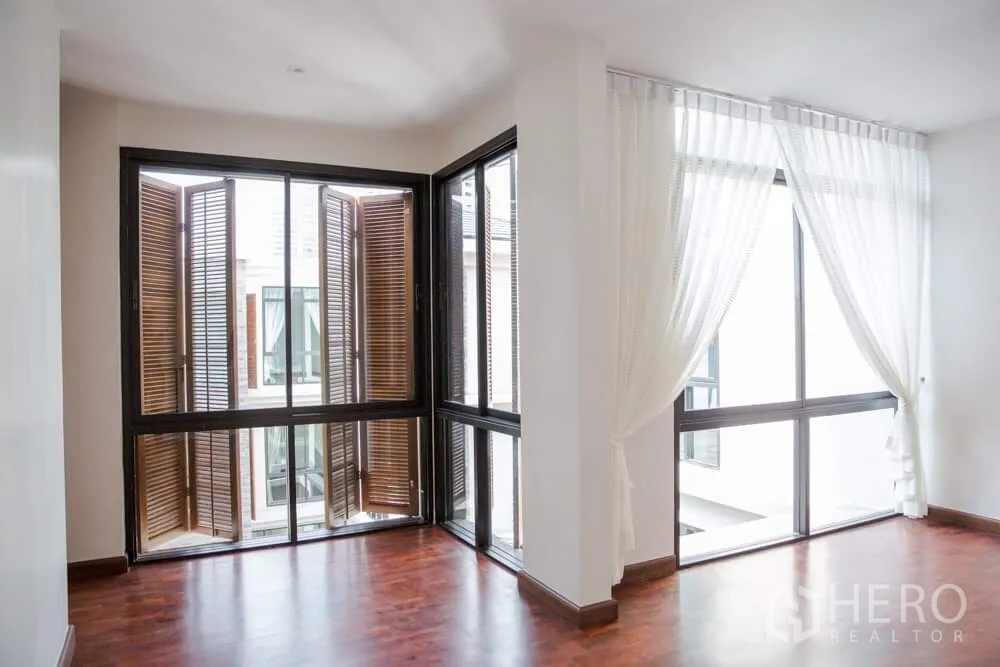 Detached House for rent in Khlong Toei, Bangkok - Sunlit room with corner windows, white curtains and wooden folding shutters.