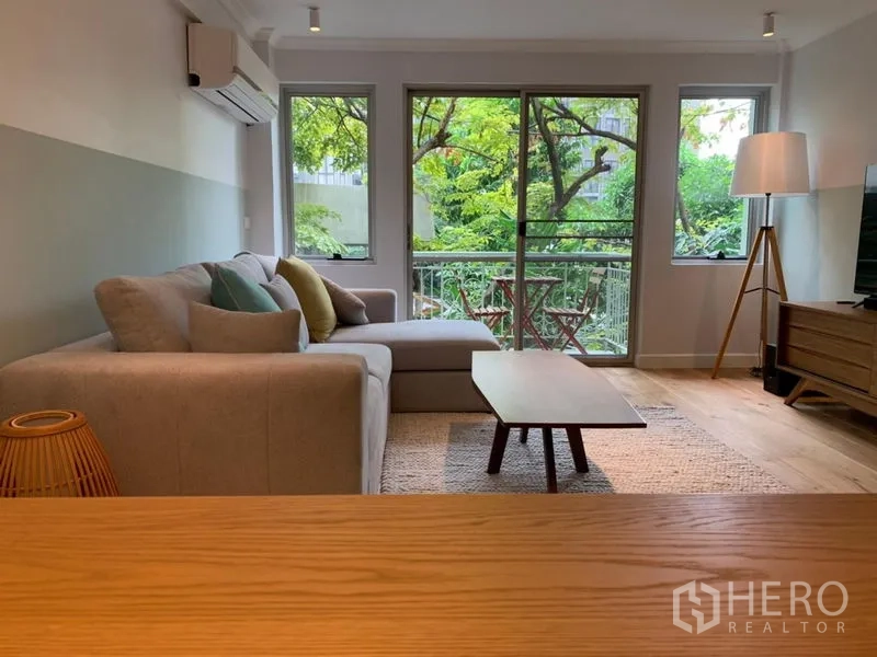 Condominium for sale in Watthana, Bangkok - Open-plan living area with sofa facing balcony and lush green view.
