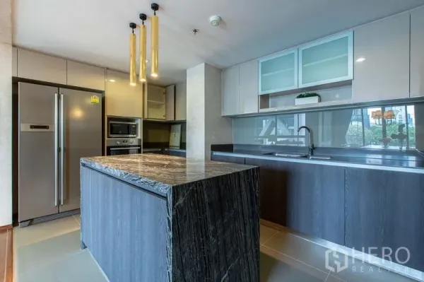 Condominium for sale in Sathon, Bangkok - Modern kitchen with dark stone island, built-in appliances and gold pendant lights.