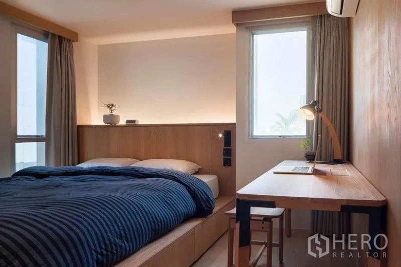 Condominium for rent in Phaya Thai, Bangkok - Cozy bedroom with platform bed, two windows and a long study desk with lamp.