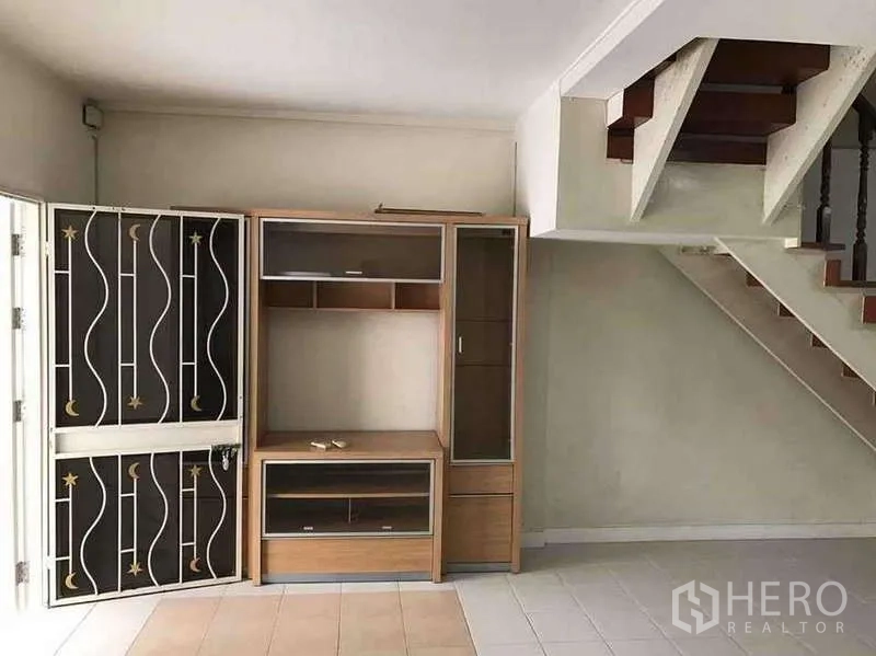 Townhouse for rent in Suan Luang, Bangkok - Living room corner with staircase and built-in TV cabinet beside a decorative metal security gate.
