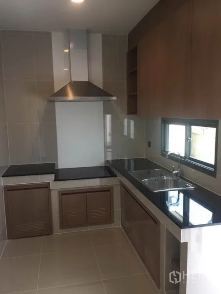 Detached House for rent in Bang Kapi, Bangkok - Fitted L-shaped kitchen with hob, stainless hood, black countertops and a side window.