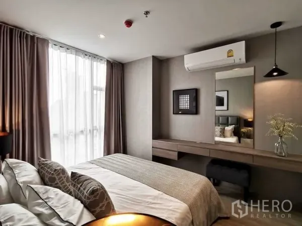 Condominium for sale in Watthana, Bangkok - Bedroom with large window and sheer curtains, built-in dressing desk, pendant lighting, and air conditioning.